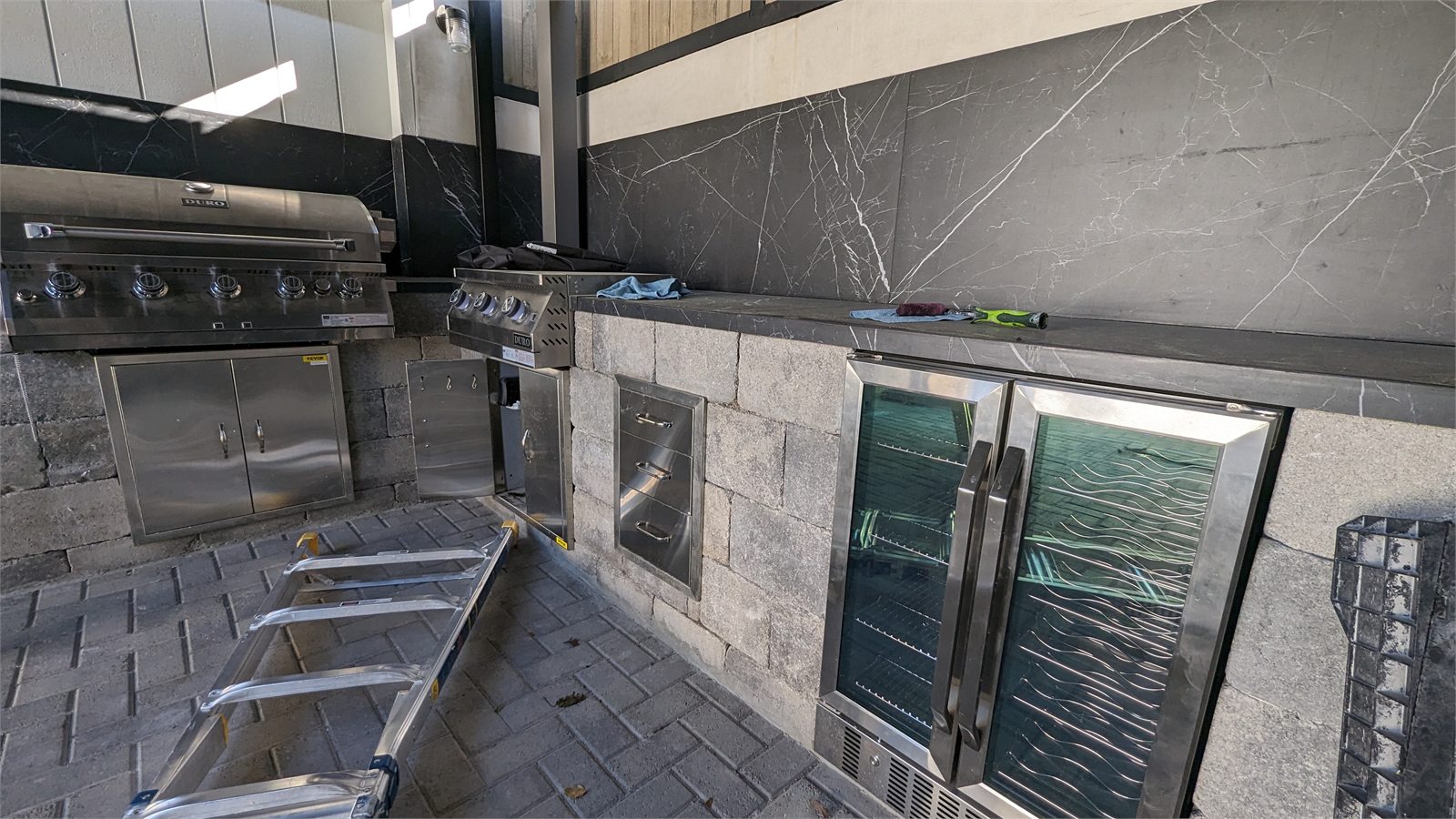 Custom outdoor kitchen with stone cladding, grill and stainless cabinetry